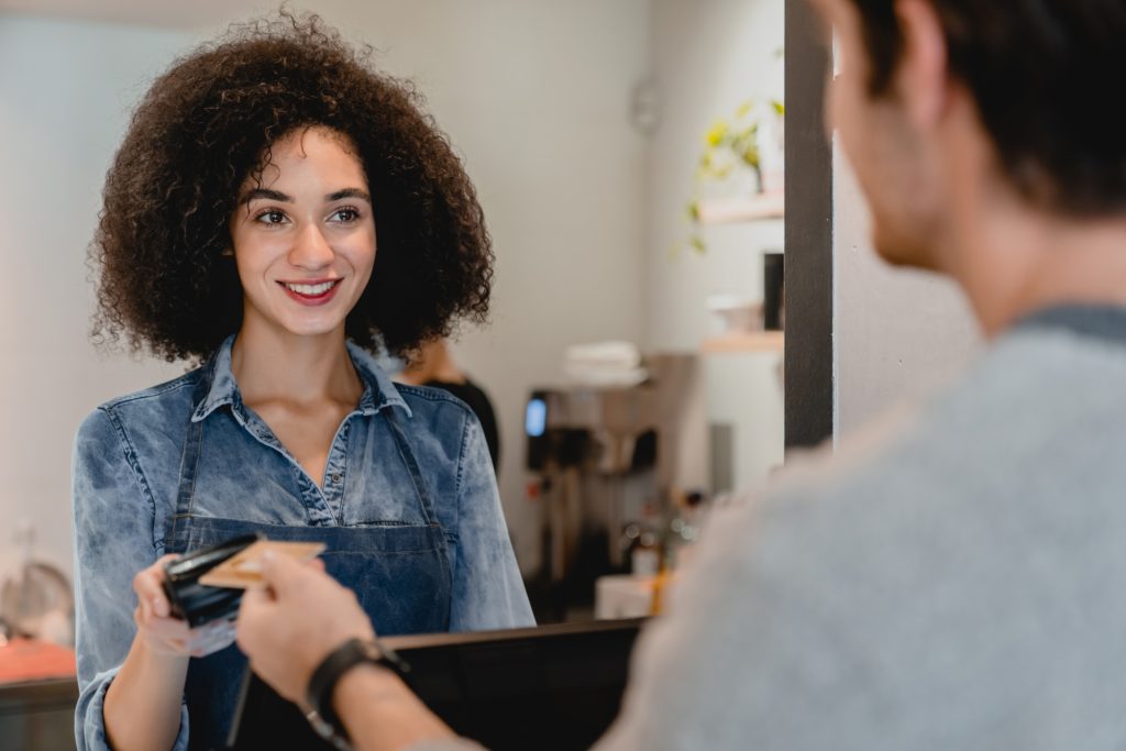 smiling attractive afro waitress servicing the customer using swiping machine in cafeteria